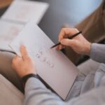 Close-up of an artist's hands sketching a face on paper with a pencil indoors.